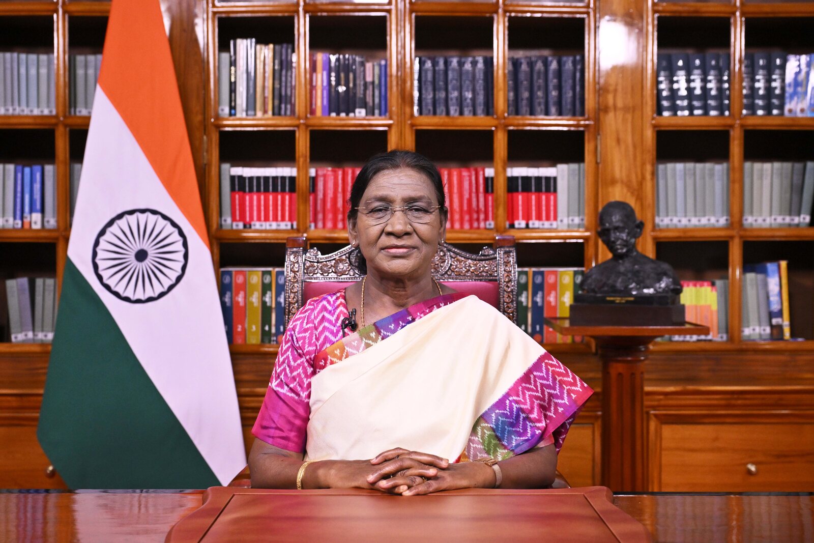 President Droupadi Murmu seated at her desk in Rashtrapati Bhavan, addressing the nation, with the national flag beside her
