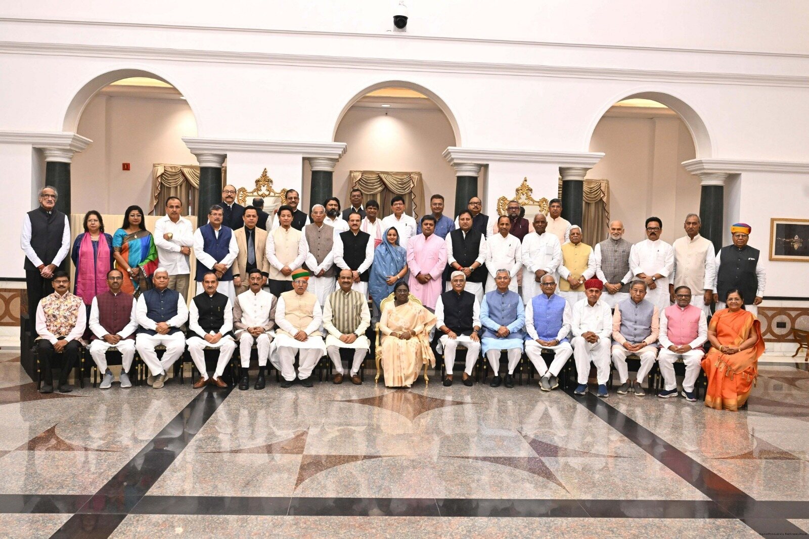 President Droupadi Murmu seated at the centre of a large official group photograph in a hall at Rashtrapati Bhavan