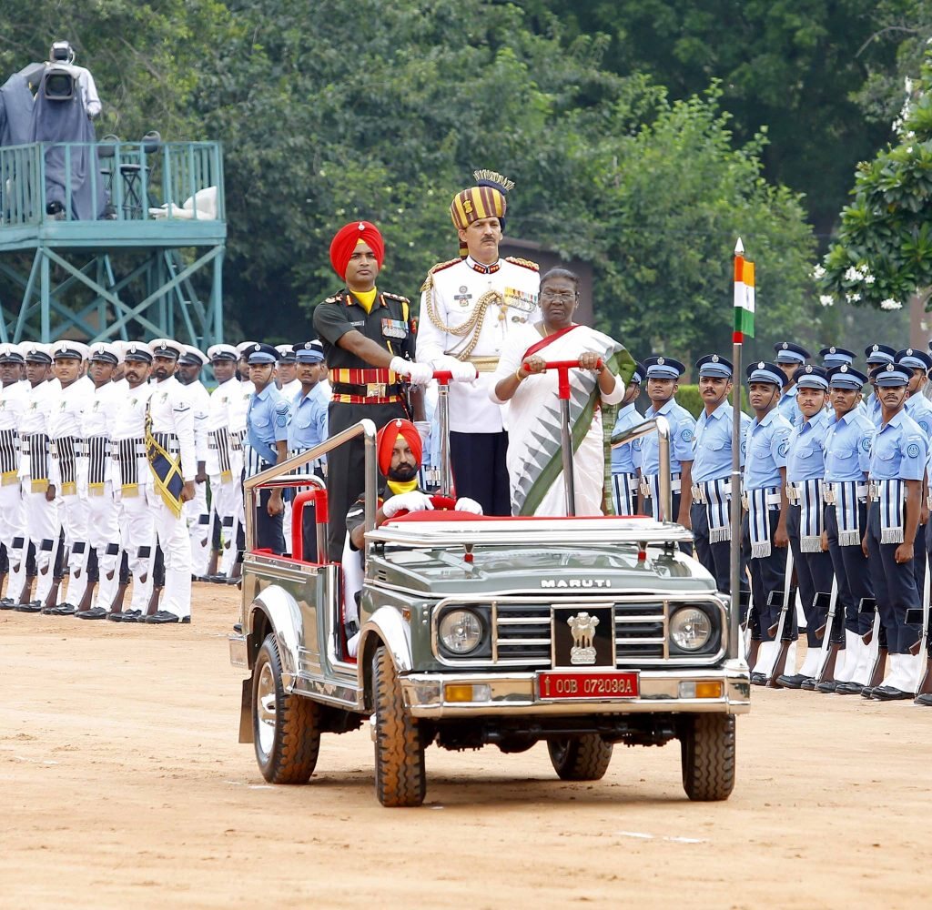 President Droupadi Murmu standing in an open ceremonial vehicle as she inspects a guard of honour formed by the three services