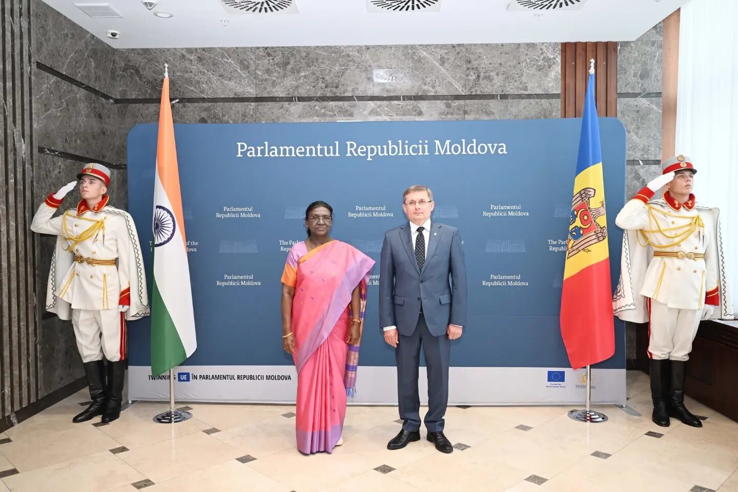 President Droupadi Murmu standing with the President of the Parliament of Moldova between the flags of India and Moldova, flanked by an honour guard